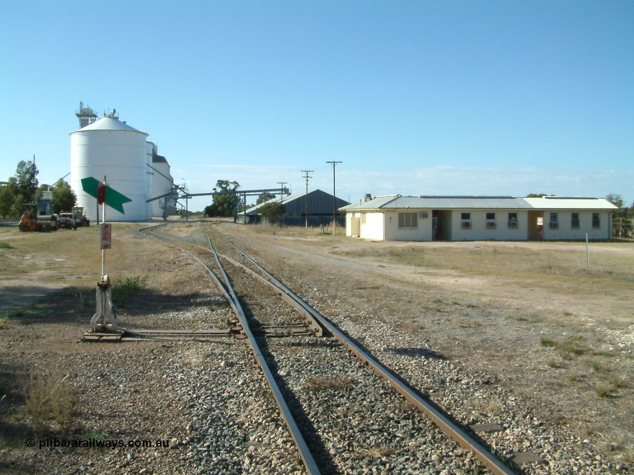 030405 160328
Lock, station yard overview, located at the 148.5 km, originally opened in May 1913 and called Terre after a local property, renamed to Lock in December 1921. Looking north along the mainline, points, lever and indicator for grain siding, Ascom style silo complex with concrete behind them, horizontal grain shed on the right with former crew barracks in front of that. 5th April 2003.
