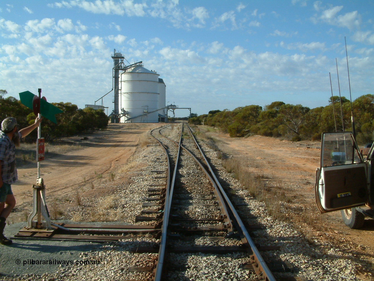 030406 082337
Murdinga, yard overview looking south down the mainline from the north end, points and point lever and indicator with Pope Searle, grain siding and silo complex with out-loading spout on gantry over both tracks. 6th April 2003.
