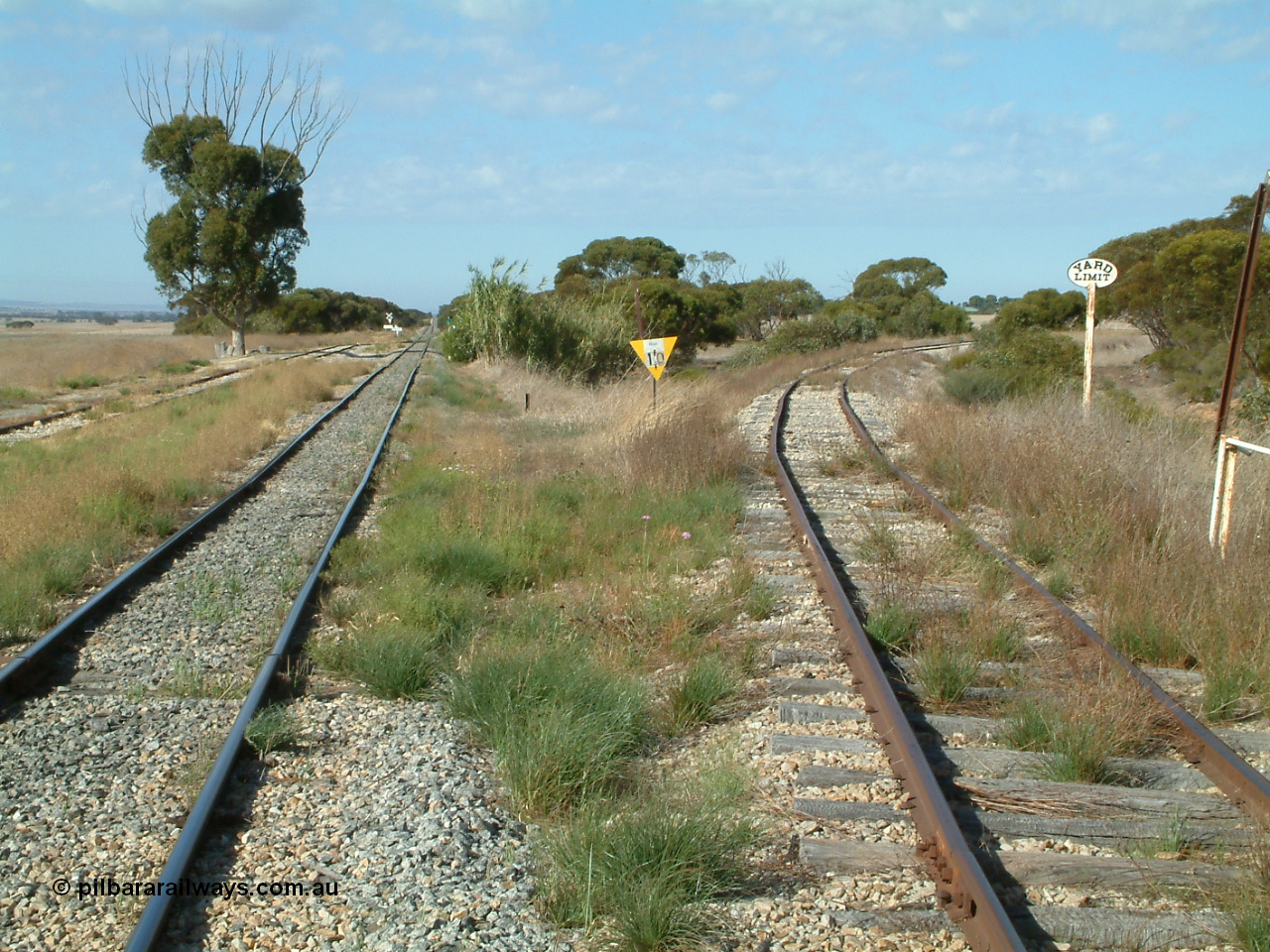 030406 092831
Yeelanna, yard view looking south, shows mainline and grain siding running south and branch line to Kapinnie and former Mount Hope branch curving away to the right across a culvert and past a cast Yard Limit sign. 6th April 2003.
