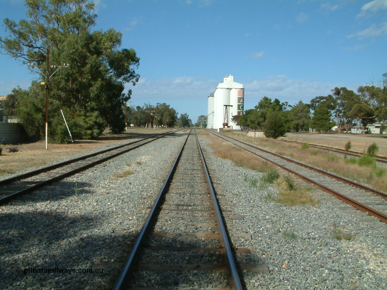 030406 094232
Cummins, yard overview looking south down the mainline through the middle of the yard. Buckleboo line on the left, with the grain and loading ramp sidings on the right. Loading ramp, rotating crane and concrete silos complexes visible in the background. 6th April 2003.
