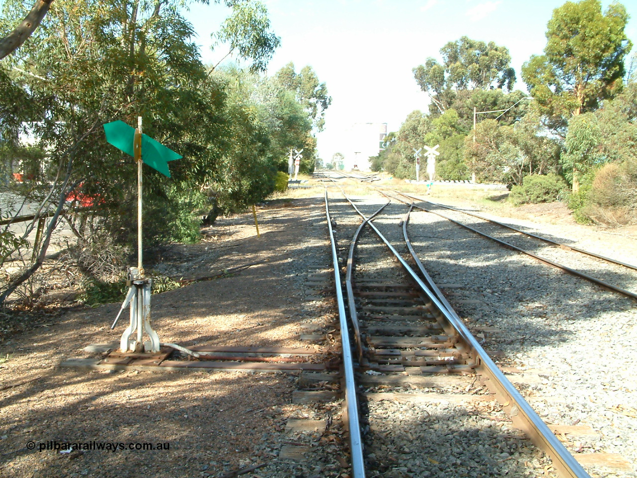 030406 094830
Cummins, yard overview looking south down the Buckleboo line with the mainline from Thevenard on the right, with points, levers and indicators for the crossover and then the grade crossing on Hall St being visible, concrete silos in the distance. 6th April 2003.
