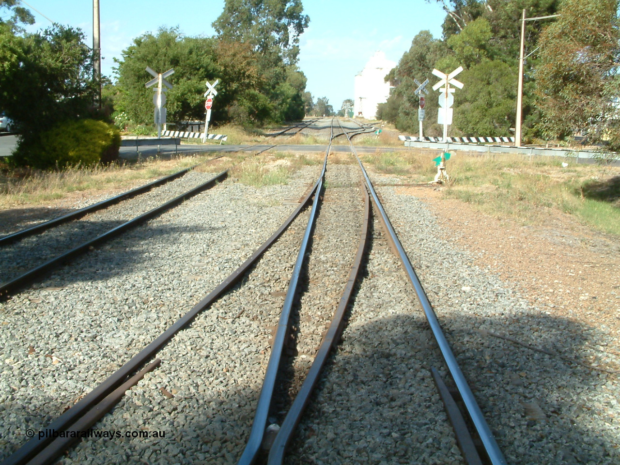 030406 094906
Cummins, yard view looking south along the mainline, points lever and indicator for the crossover to the Buckleboo line visible, Hall St grade crossing, then the points and levers for the grain and goods loading ramp sidings beyond. Buckleboo line is on the left. 6th April 2003.
