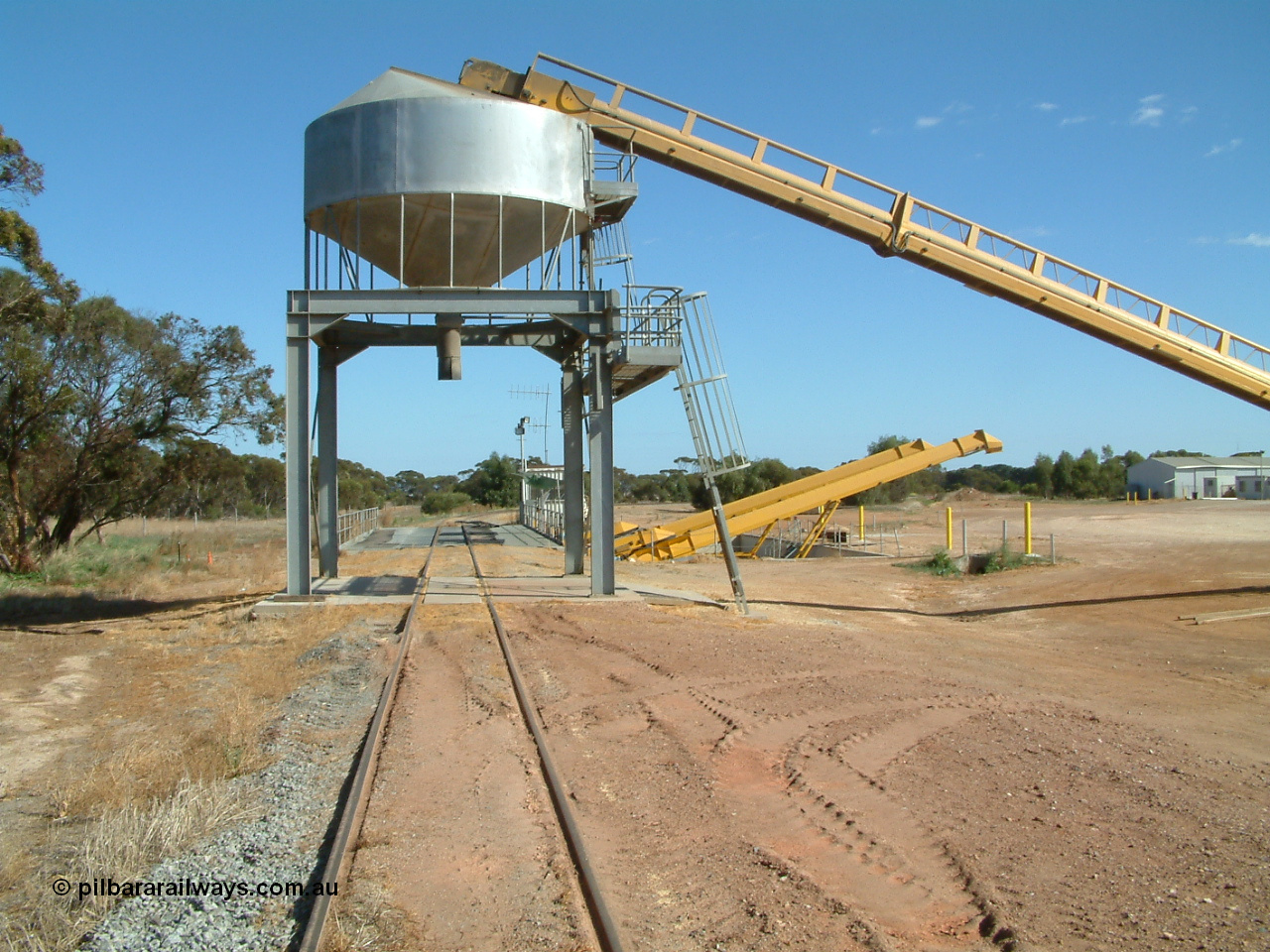 030406 100902
Cummins, view of the grain bunker rail unloading facility with dual DOH 'Drive Over Hopper' and stackers for loading road vehicles and with the original overhead outflow bin and feed conveyor for loading rail waggons. 6th April 2003.
