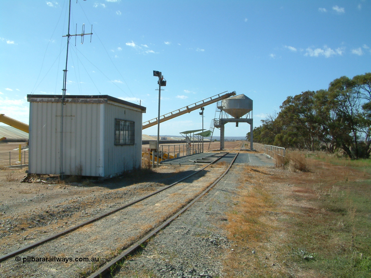 030406 101028
Cummins, view looking from Cummins of the grain bunker rail unloading facility with dual DOH 'Drive Over Hopper' and stackers for loading road vehicles and with the original overhead outflow bin and feed conveyor for loading rail waggons. Loaded bunkers visible on the left. 6th April 2003.
