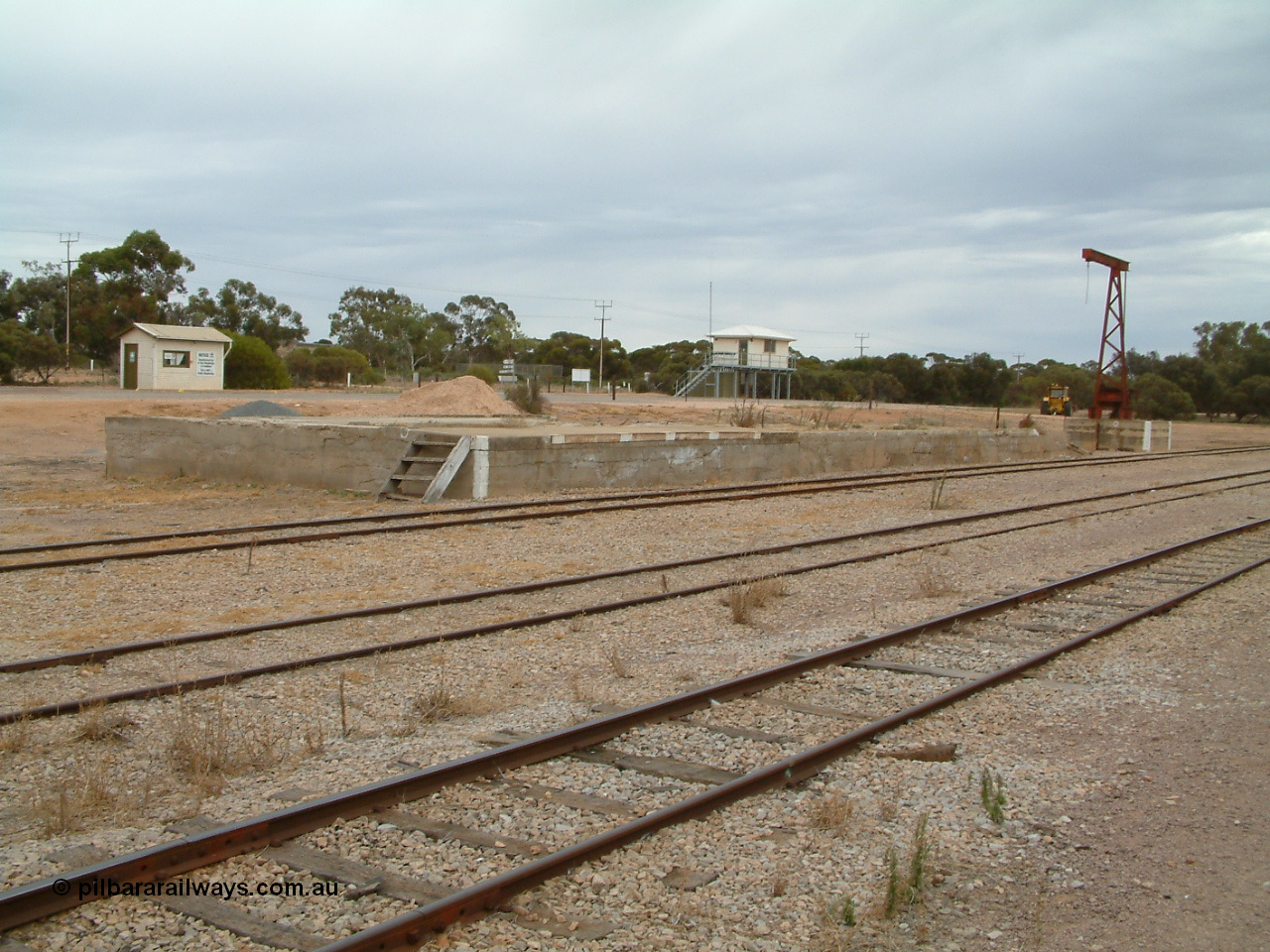 030407 094425
Minnipa, yard view of loading ramp and former site of goods shed, rotating jib crane and road vehicle weighbridge scale room and grain truck sampling building in the background. 7th April, 2003.

