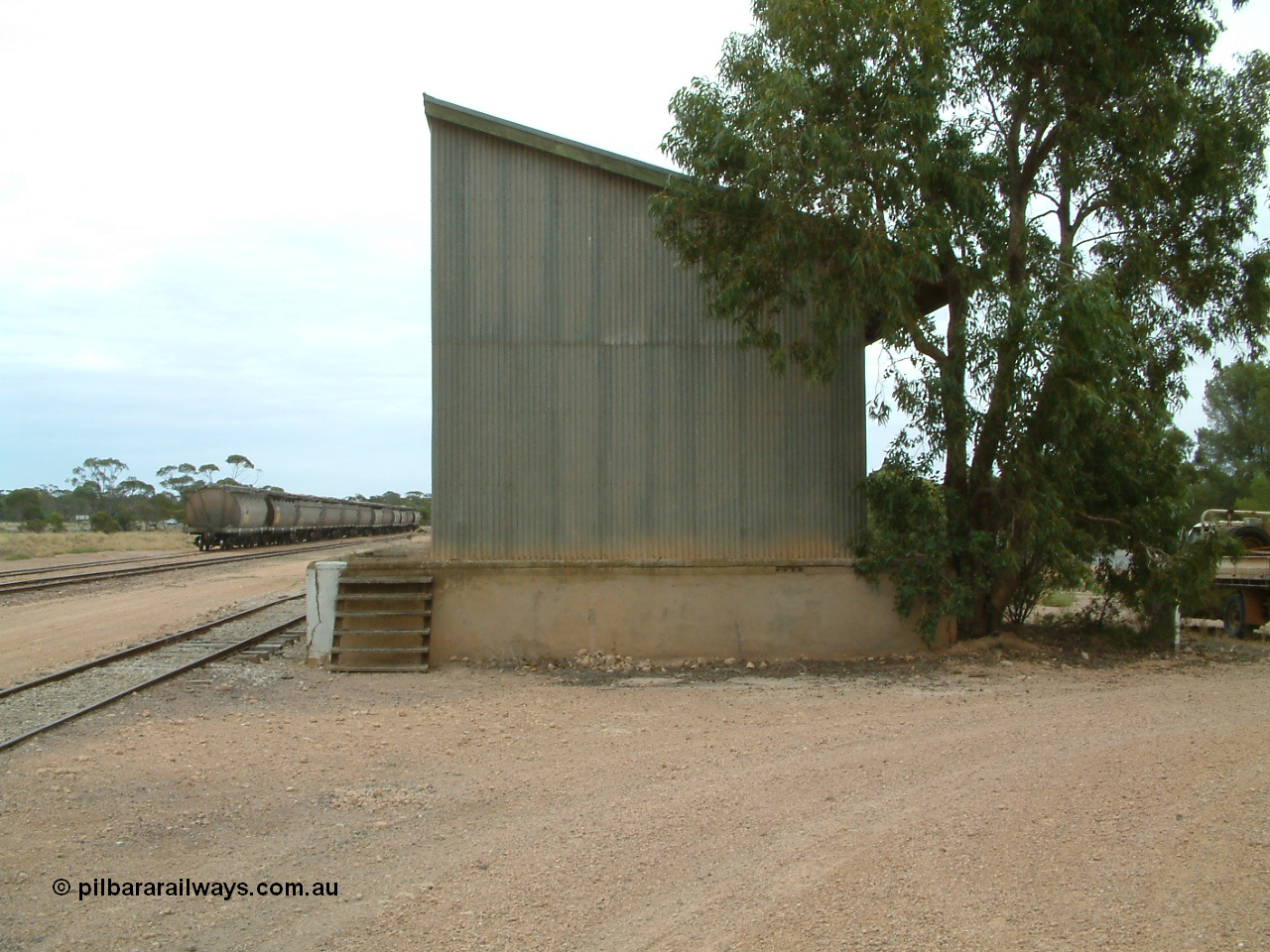 030407 104921
Poochera, south elevation of goods shed and platform, loaded rake of grain waggons awaits pick in the background. 7th April 2003.
