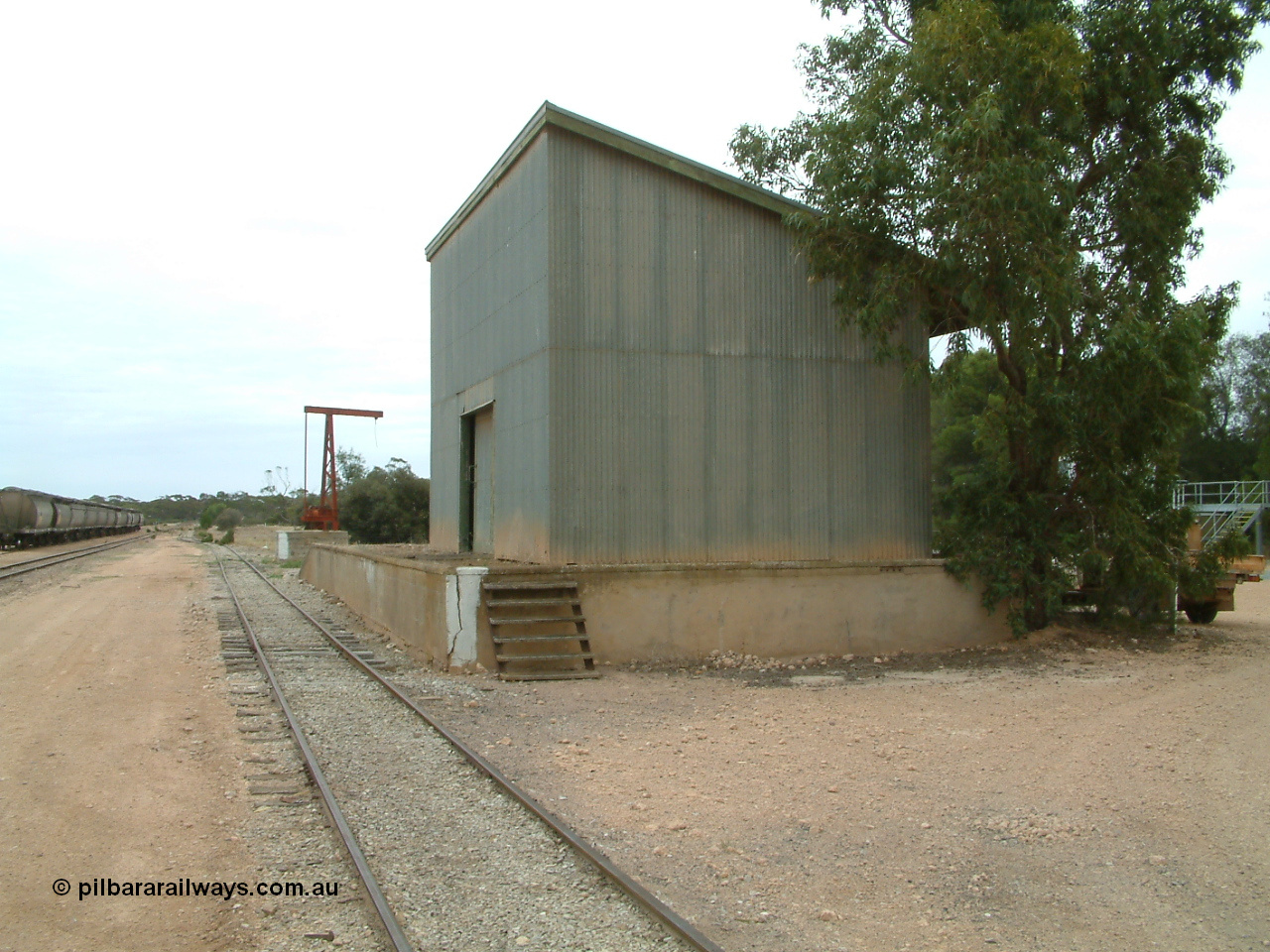 030407 104934
Poochera, south western elevation of goods shed and platform with rotating jib crane in the distance, loaded rake of grain waggons awaits pickup to the left. 7th April 2003.
