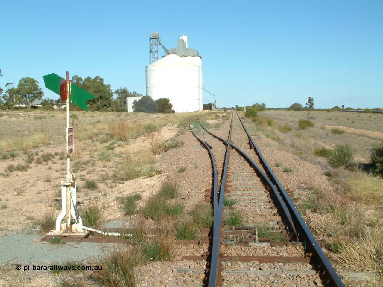 030411 160238
Cungena, 306.7 km, yard overview looking south from Thevenard end, Ascom style silo complex block 2 with concrete block 1 behind it. Station shelter visible behind tree.
