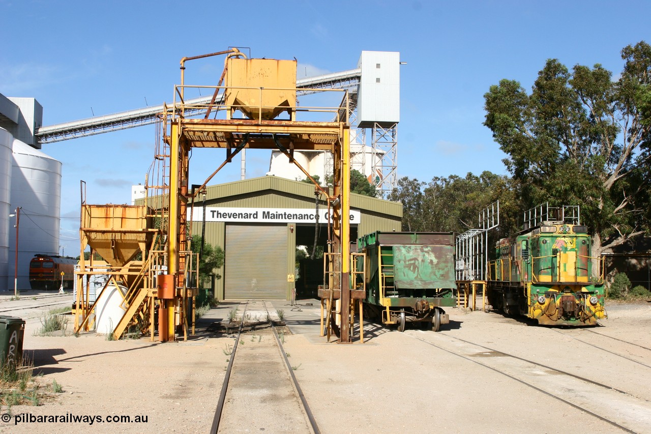 060113 2452
Thevenard Maintenance Centre overview, AE Goodwin ALCo model DL531 830 class locomotive 871 serial G3422-1 was issued when built in 1966 to the Eyre Peninsula division of South Australian Railways. Still wearing Australian National green and yellow but with ASR decals as it stands in the yard with a couple of ENH type hopper waggons. Empty train 6DD3 sneaks beside the no longer rail served grain silos at left. 13th January 2006.
