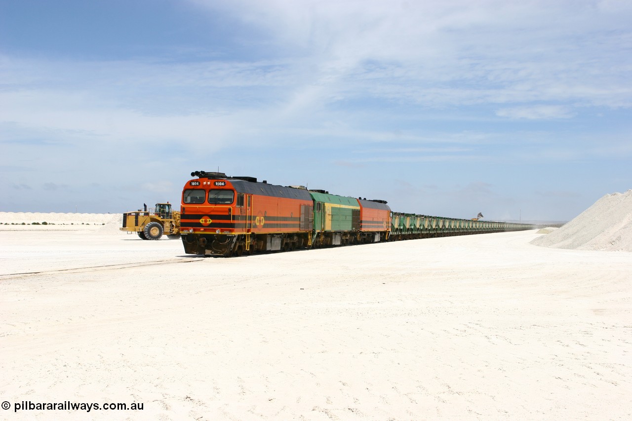 060113 2554
Kevin, narrow gauge locos 1604, NJ 3 and 1601 wait while their return working train 6DD4 is loaded on the mainline to Thevenard. The plant is behind the tipping loader and Kevin back around to the right behind the gypsum pile. 13th January 2006.
