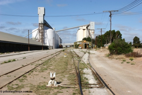060113 2459
Thevenard, yard view looking west from No. 13 points at the front of the maintenance 'yard' with the disused grain bunker and 6DD3 running along beside the silos as it unloads at GRA, further silos form the background with the maintenance centre with stand-by loco 871 on hand and a couple of ENH hopper waggons. January 13, 2006.
