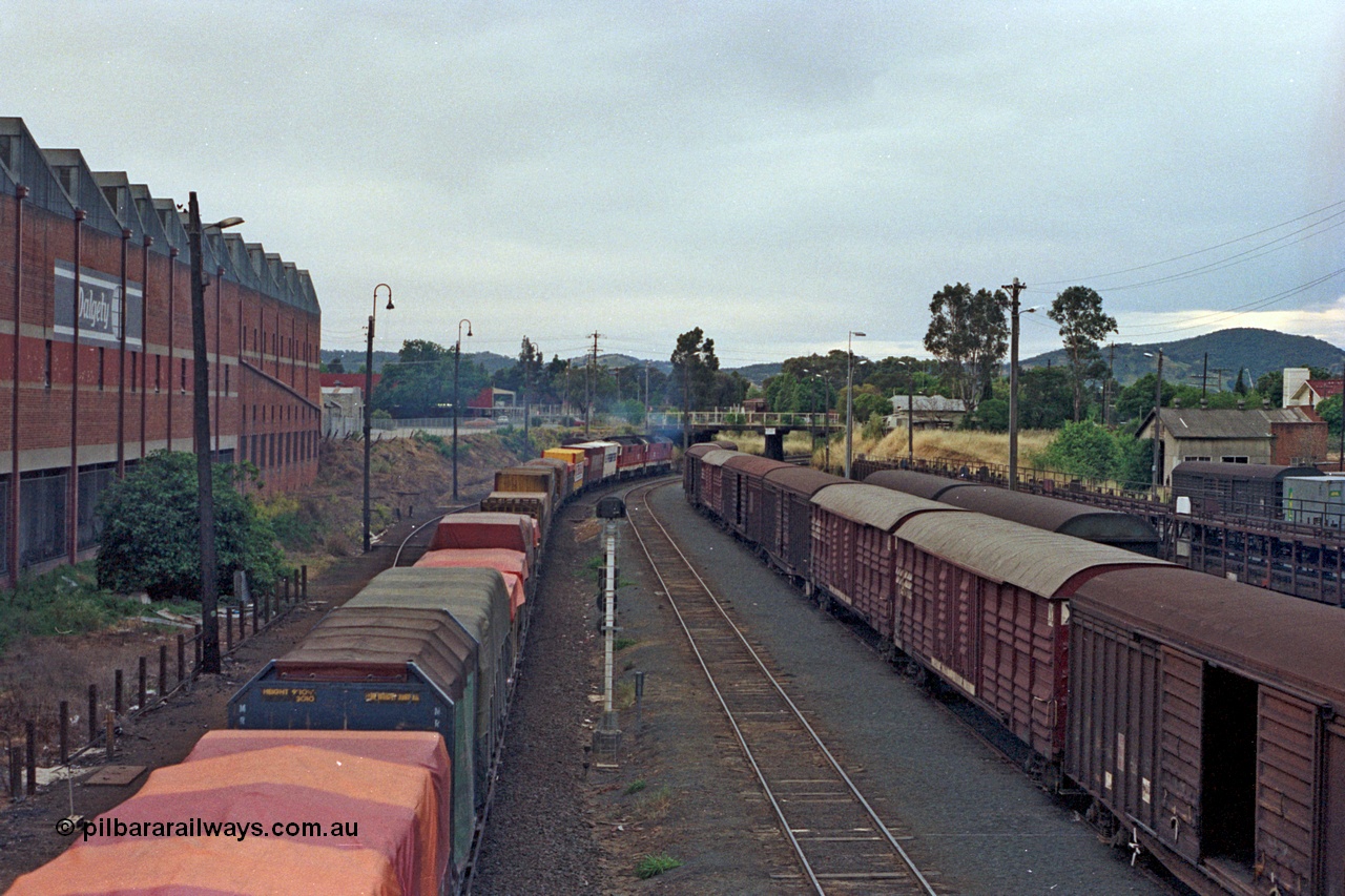 100-04
Albury yard view, Sydney bound goods, trailing shot, looking north, from Wilson Street footbridge, old Dalgety's building on the left, signal post AY61, louvre vans and motorail waggons on the right. [url=https://goo.gl/maps/nngpTA37VQekQpCt7]Geodata[/url].
