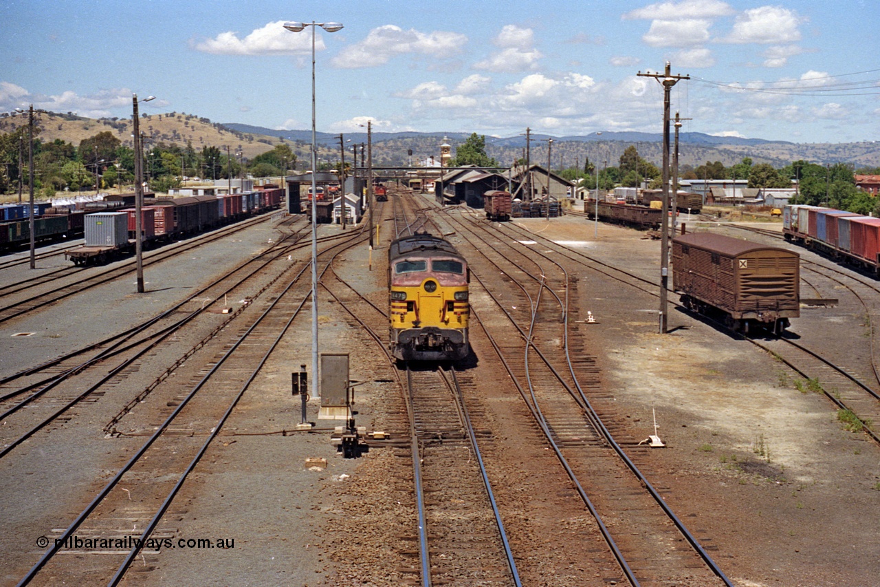 100-13
Albury station yard overview looking south from Wilson Street footbridge, NSWSRA standard gauge 44 class 4479 AE Goodwin ALCo model DL500B serial G3421-19 readies for Inter-Capital Daylight banker duty, 2 lever ground frame and point rodding, loco shops, station building and goods sheds visible, broad gauge tracks at far right with container waggons. [url=https://goo.gl/maps/nngpTA37VQekQpCt7]Geodata[/url].
Keywords: 44-class;4479;AE-Goodwin;ALCo;DL500B;G3421-19;