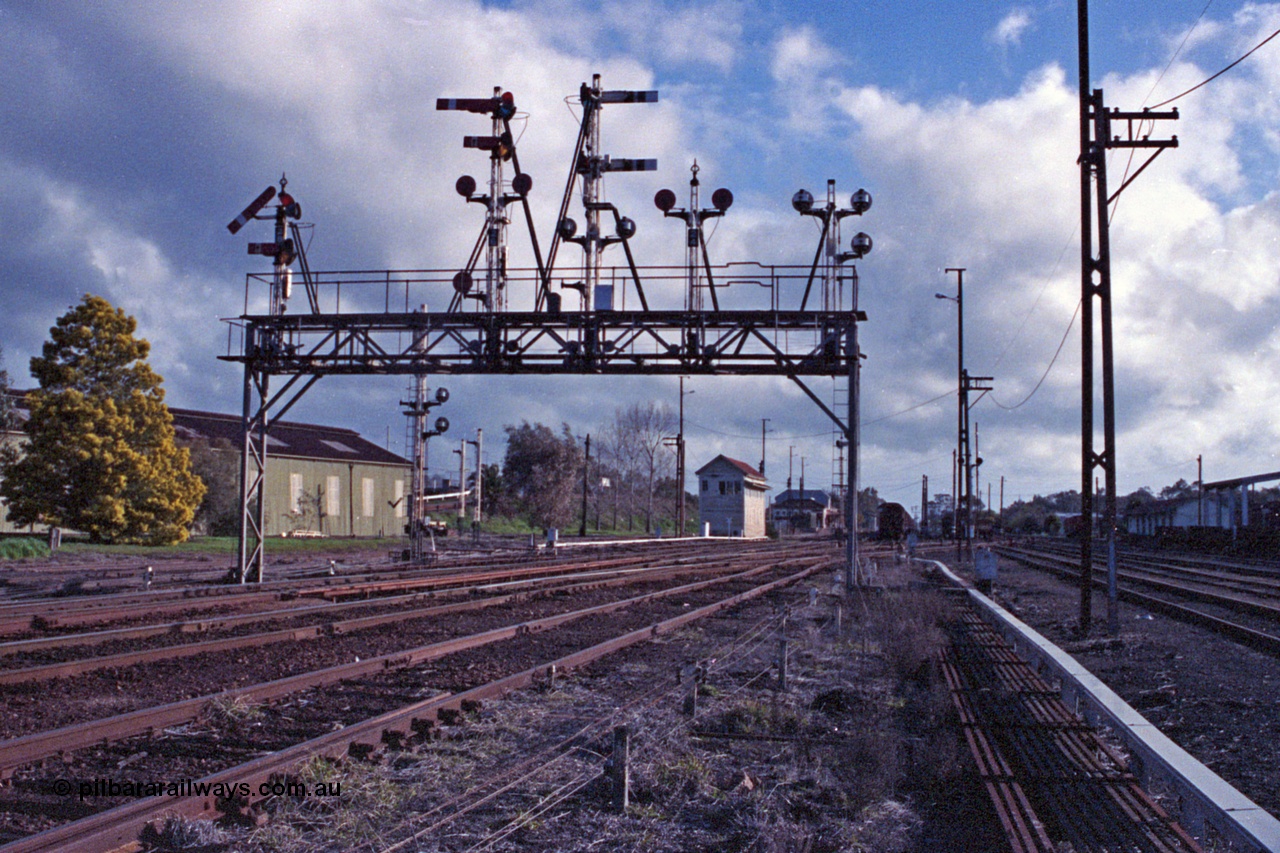 103-23
Benalla station yard overview, signal gantry still complete and intact, semaphore signal post 28 pulled off for up Albury pass, looking south, before rationalisation, workshops at left, Benalla B signal box, point rodding and signal wires, Freightgate canopy at right.
