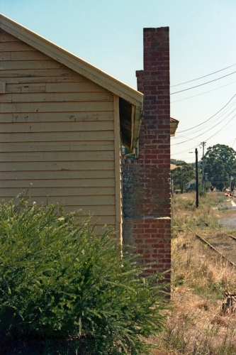 105-18
Wallan, station platform 2 waiting room, brick chimney, and south end wall, point rodding, signal wires and No.3 Rd in the grass.
