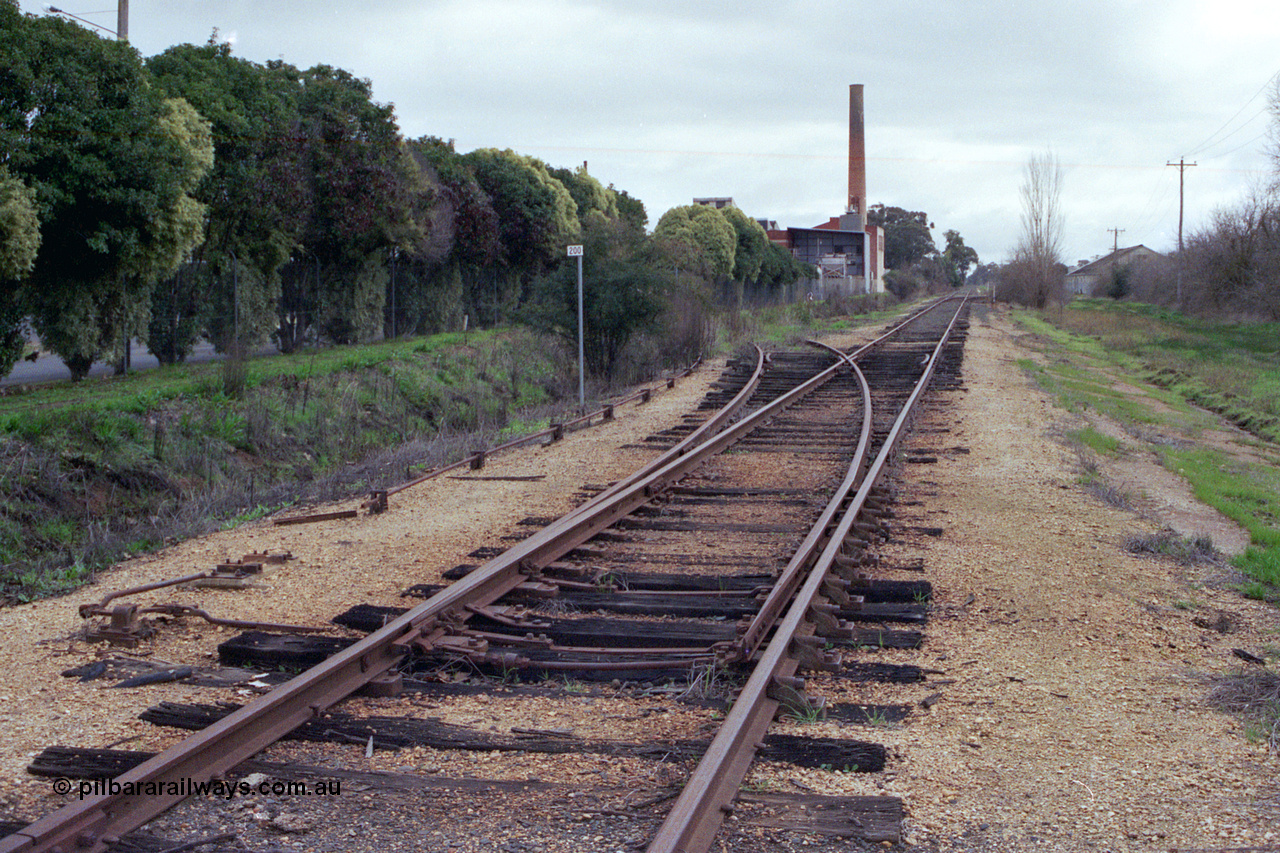 107-01
Kyabram track view looking north, 200 km post, Kyabram Co-op Fruit Preserving Company and Southern Can Company sidings on the left, point rodding and points spiked for normal, Kyabram Fruit Packers siding on the right in the background.
