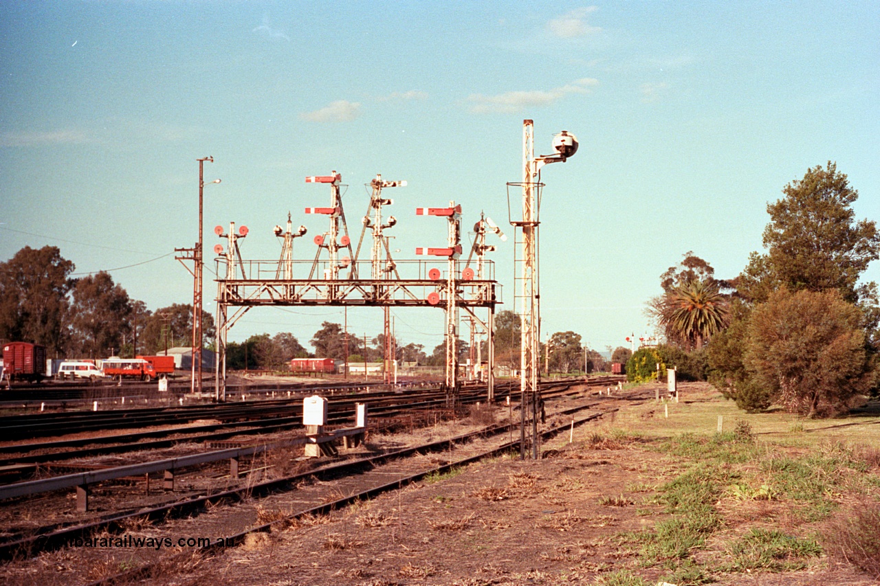 114-25
Benalla signal gantry, semaphore signal post 28 pulled off for up Albury passenger train, looking north, yard still fully interlocked and signalled, disc signal post 22 facing away from camera, post 27 facing camera, signal gantry features from left, disc post 23, 24, semaphore post 25, 26 and 28.
