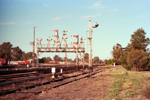 114-25
Benalla signal gantry, semaphore signal post 28 pulled off for up Albury passenger train, looking north, yard still fully interlocked and signalled, disc signal post 22 facing away from camera, post 27 facing camera, signal gantry features from left, disc post 23, 24, semaphore post 25, 26 and 28.
