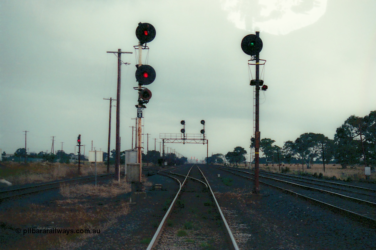 115-28
Somerton, standard gauge crossing loop, track overview, searchlight signal posts, SOM-8 up home for Somerton Loop, E798 up broad gauge signal, signal gantry for crossing loop, looking south, standard gauge siding to Blue Circle Cement and shunt signal 7 at left, broad gauge running lines on right.
