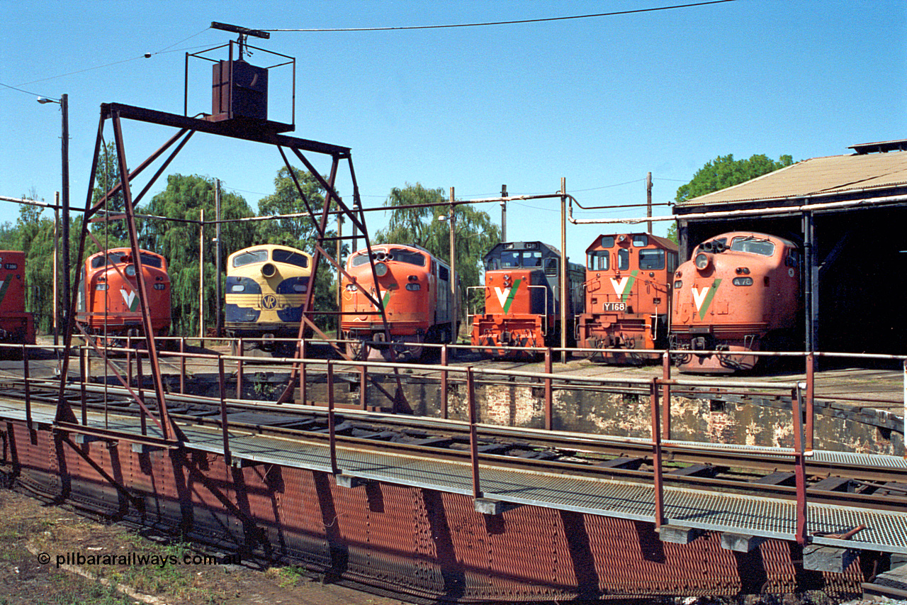 122-07
Traralgon loco depot, turntable, V/Line broad gauge locos are left to right and all Clyde Engineering EMD models; A class A 77, AAT22C-2R serial 83-1181 rebuilt from B 77, ML2 serial ML2-18. B class B 75, ML2 serial ML2-16 still in VR livery. A class A 81 serial 85-1189 rebuilt from B 81 serial ML2-22. T class T 381, model G8B serial 64-336. Y class Y 168 model G6B serial 68-588. A class A 78 serial 84-1185 rebuilt from B 78 serial ML2-19. March 1992.
