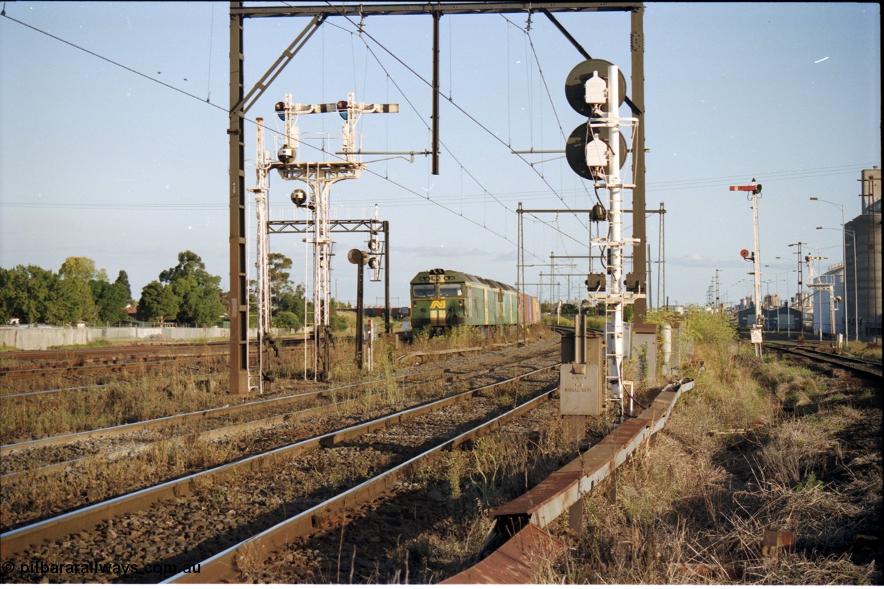 124-16
Sunshine looking from the passenger lines across to the Independent Through Goods lines, disc and semaphore signal posts 31 and 31B for control of the Independent Trough Goods lines, down Adelaide broad gauge goods train waiting to cross over the passenger lines, BL classes Clyde Engineering EMD model JT26C-2SS serial 83-1014 and BL 35 Clyde Engineering EMD model JT26C-2SS serial 83-1019 in AN livery, standard gauge Sunshine Loop to the left of train.
