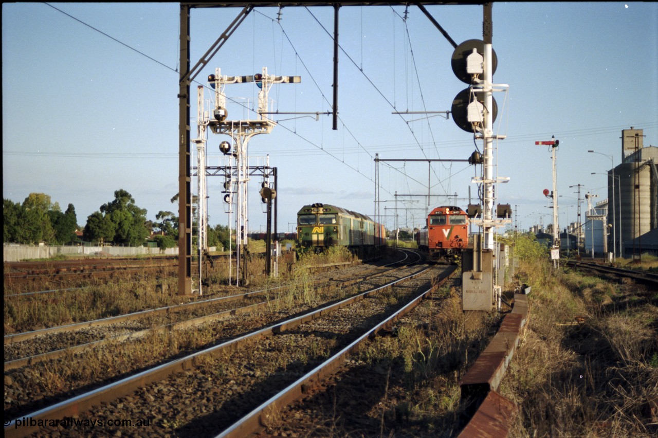 124-17
Sunshine looking from the passenger lines across to the Independent Through Goods lines, signal post 71 at camera, disc and semaphore signal posts 31 and 31B for control of the Independent Trough Goods lines, down Adelaide broad gauge goods train waiting to cross over the passenger lines, BL classes Clyde Engineering EMD model JT26C-2SS serial 83-1014 and BL 35 Clyde Engineering EMD model JT26C-2SS serial 83-1019 in AN livery, standard gauge Sunshine Loop to the left of train, V/Line broad gauge down passenger train with N class N 471 Clyde Engineering EMD model JT22HC-2 serial 87-1200 'City of Benalla' passing on passenger lines, Newport Loop Line and GEB sidings at far right.
Keywords: N-class;N471;Clyde-Engineering-Somerton-Victoria;EMD;JT22HC-2;87-1200;