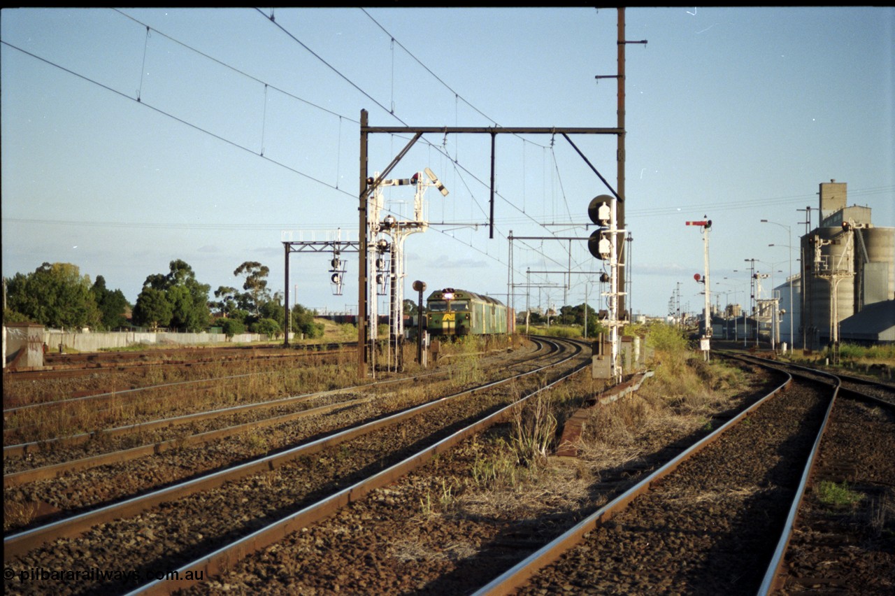 124-18
Sunshine looking from the passenger lines across to the Independent Through Goods lines, signal post 71 at camera, disc and semaphore signal posts 31 and 31B for control of the Independent Trough Goods lines, 31B pulled off for down Adelaide broad gauge goods train to cross over the passenger lines, BL classes Clyde Engineering EMD model JT26C-2SS serial 83-1014 and BL 35 Clyde Engineering EMD model JT26C-2SS serial 83-1019 in AN livery, standard gauge Sunshine Loop to the left of train, Newport Loop Line and GEB sidings at far right.
Keywords: BL-class;BL30;Clyde-Engineering-Rosewater-SA;EMD;JT26C-2SS;83-1014;