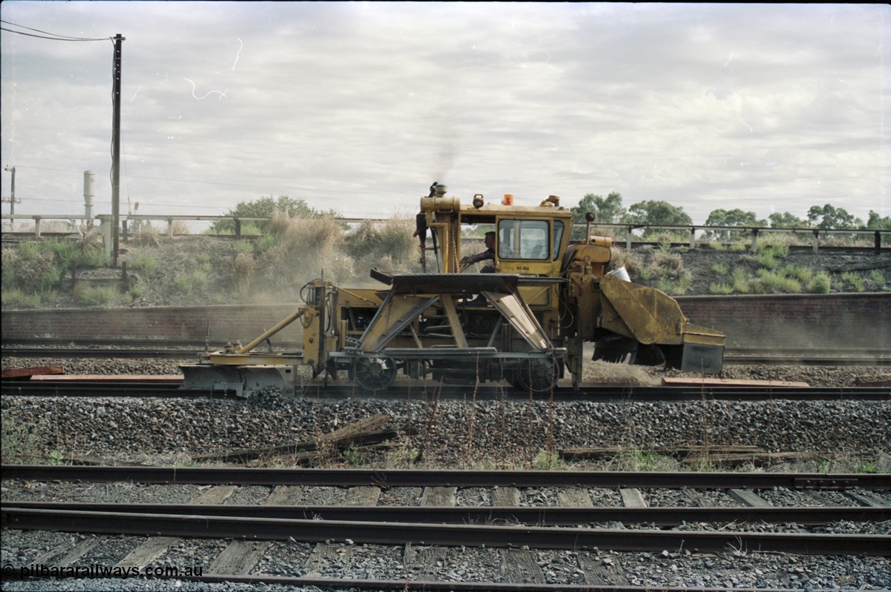 125-09
Seymour, standard gauge mainline, ballast regulator working past loco depot.
