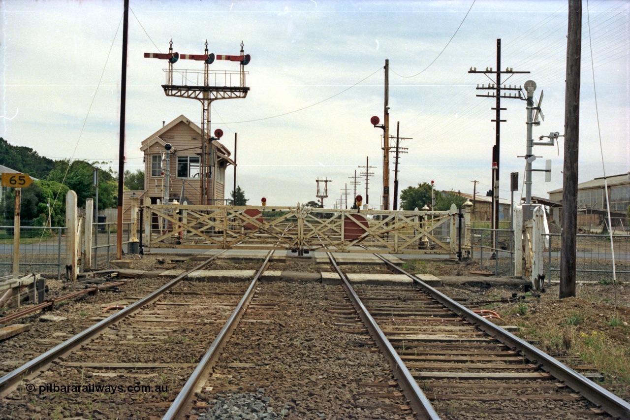 128-05
Ballarat, Linton Junction or Ballarat D signal box, looking west, gates about to be replaced with booms, semaphore triple doll signal Post 20 with disc for Timken's Siding, the three dolls are Cattle Yard Line, Linton Line and Ararat Line, and disc signal Post 21 for Timken's Siding, semaphore signal Post 23 in the distance, the 'ships wheel' in the signal box window is for operating the interlocked gates.
