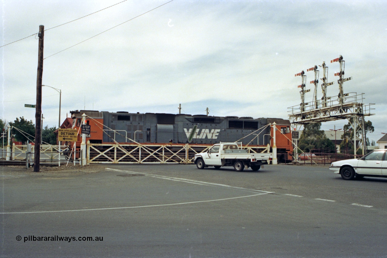 128-15
Ballarat Station, Lydiard St or B signal box, view across Lydiard Street grade crossing with interlocked gates closed, signal gantry with semaphore signal posts 26 to 29, V/Line broad gauge N class N 464 'City of Geelong' Clyde Engineering EMD model JT22HC-2 serial 86-1193 shunts around train crossing Lydiard Street.
Keywords: N-class;N464;Clyde-Engineering-Somerton-Victoria;EMD;JT22HC-2;86-1193;