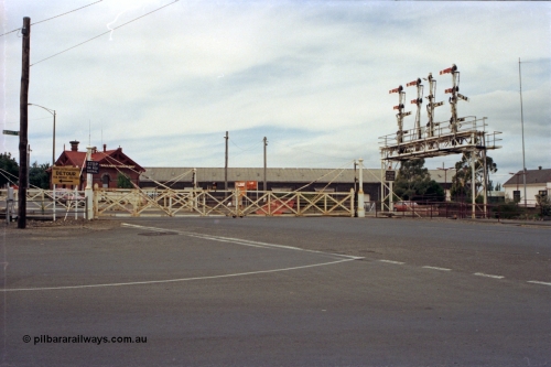 128-14
Ballarat Station, Lydiard St or B signal box, view across Lydiard Street grade crossing with interlocked gates closed, signal gantry with semaphore signal posts 26 to 29, post 26 pulled off for shunt, looking north, Ballarat Coachlines building and Ballarat yard goods shed in the distance.
