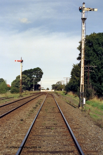 128-18
Gisborne, station overview looking south, semaphore signal Posts 4 and 5, crossover and Up Refuge Siding, Gisborne Road grade crossing non-interlocked swing gates and station in the distance looking towards Melbourne in the up direction.
