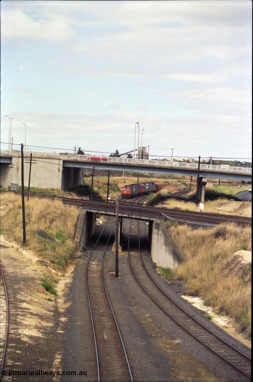 133-13
North Geelong, V/Line broad gauge G class locos G 524 Clyde Engineering EMD model JT26C-2SS serial 86-1237 and G 528 serial 88-1258 work a loaded grain train under the Geelong Road bridge, bound for the grain loop, the track on the right is the grain loop departure road, the lines to Geelong are on the bridge.
