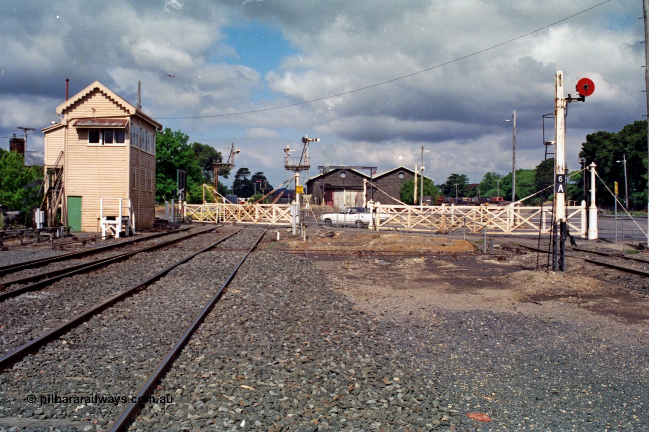 139-08
Ballarat East Signal Box looking east across Humffray Street with the interlocked gates for the double track mainline to Warrenheip and another set for the loco tracks protected by Post 6A which was installed following its removal from Beaufort, bluestone goods shed with stored T class locomotives in the distance with the loco depot behind. Disc 6A is for movements across Humffray Street to Loco with Disc 6 for departing movements. Disc signal Post 5A on the left for down trains from No. 1 Road to the Goods Arrival Road or Siding Y, double bracket Post 5 (with removed right Arm) left had Arm is from No. 2 Road to Passenger Line to Post 11 and controlled from A Box, the staff exchange platform is for the former line to Buninyong.
