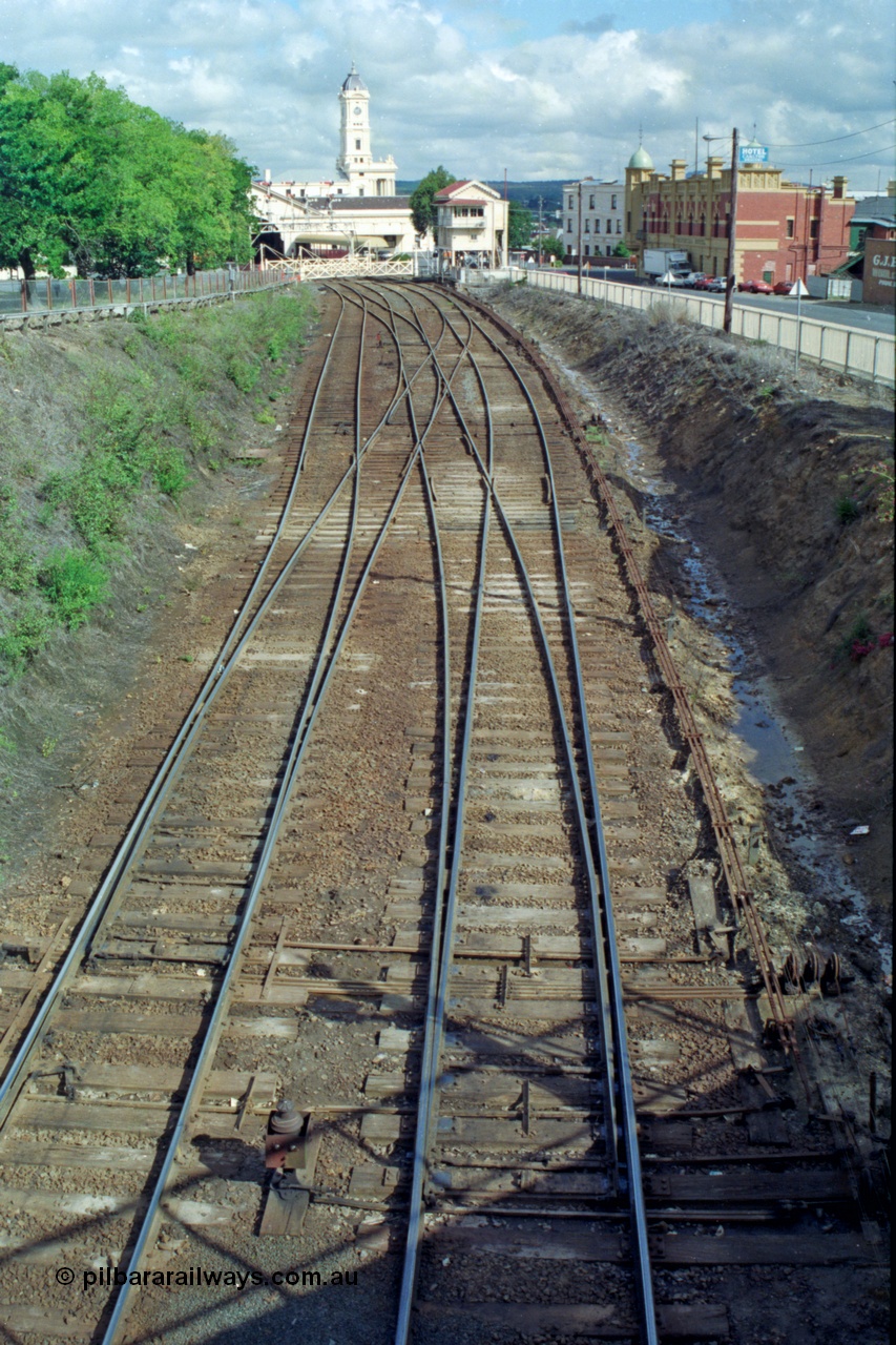 139-16
Ballarat station junction, track view of the junction at Ballarat B signal box or Lydiard Street box, looking east from the Armstrong Street bridge, double track to triple track which used to then become four tracks on the other side of the gates before No. 2 Road was removed. The shadow of Disc Post 33 can be seen along with the interlocking of the points with the signal pulleys.
