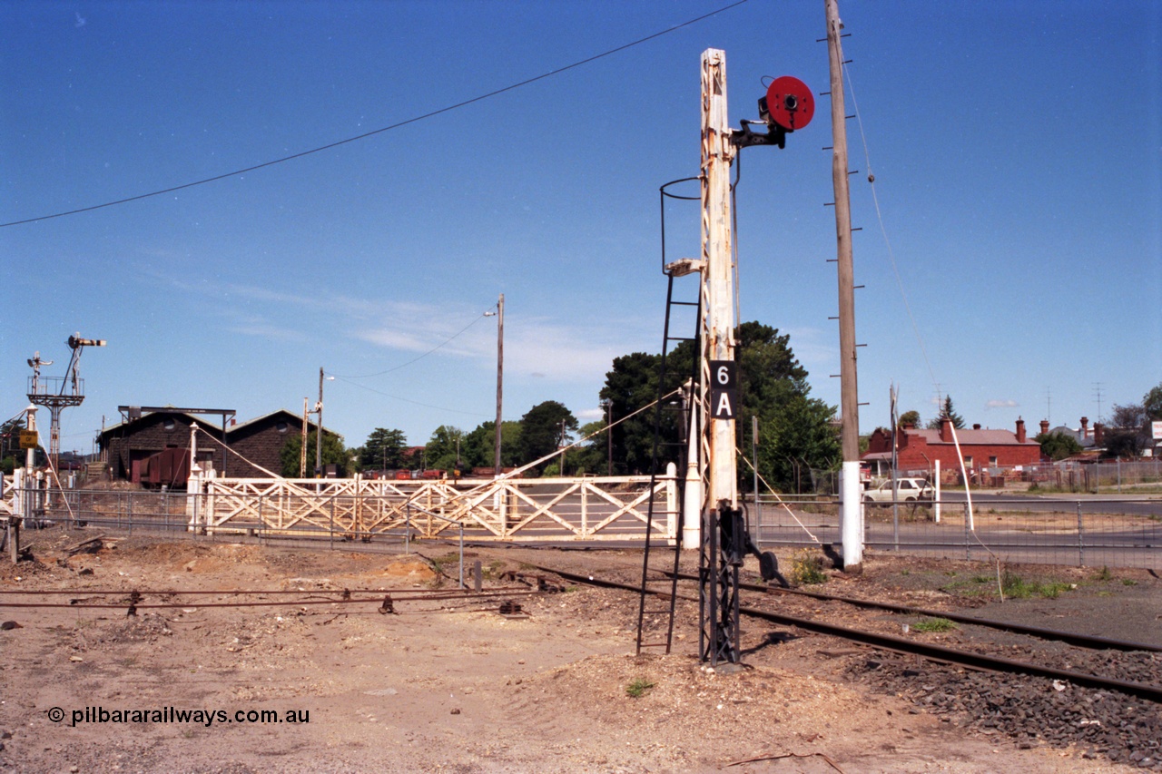 140-1-05
Ballarat East yard view, disc signal post 6A stands sentinel to the entry to Ballarat East Loco Depot with the second set of interlocked gates for the crossing of Humffray St, goods sheds in the background.
