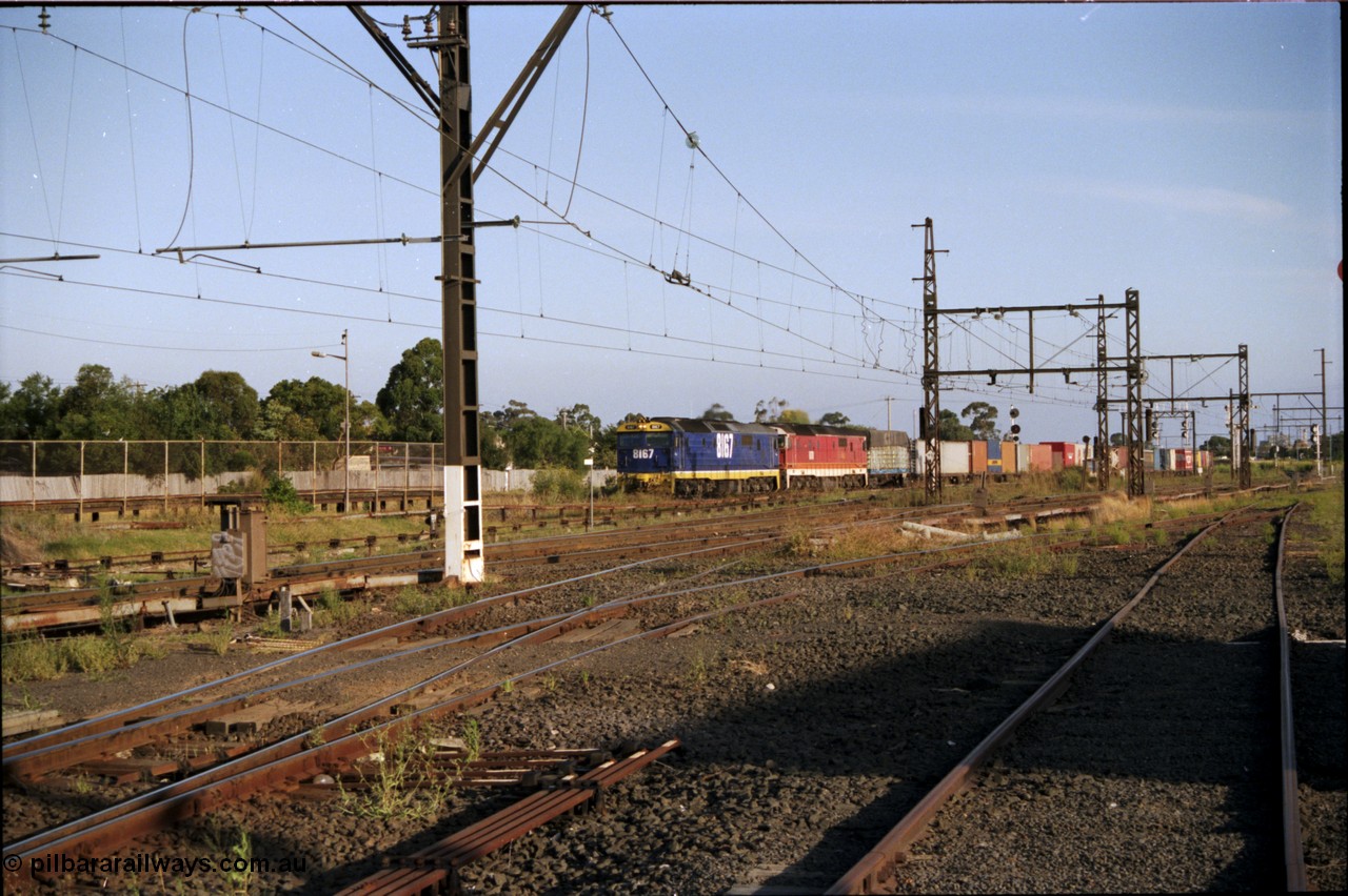 141-1-01
Sunshine, standard gauge NSWSRA State Rail 81 class locos 8167 Clyde Engineering EMD model JT26C-2SS serial 85-1086 in the Freight Rail stealth livery and another in the candy livery lead a down north bound goods train away from Sunshine Loop, view across broad gauge tracks from the former goods yard, point rodding.
Keywords: 81-class;8167;Clyde-Engineering-Kelso-NSW;EMD;JT26C-2SS;85-1086;