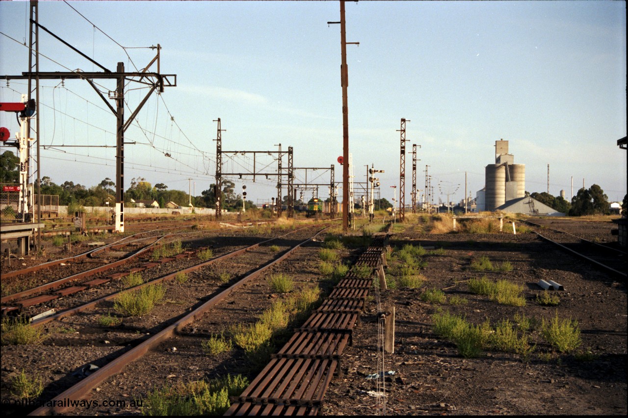 141-1-02
Sunshine, distant view of a broad gauge down Adelaide goods train with an Australian National BL class leading a V/Line G class, as they run along the Independent Through Lines, the abundant array of signals and point rodding that make up the mechanically interlocked and signalled Sunshine area are visible, along with the GEB sidings and silos on the right, the lines to Tottenham curve round to the left, while straight up is the Newport Loop Line.
