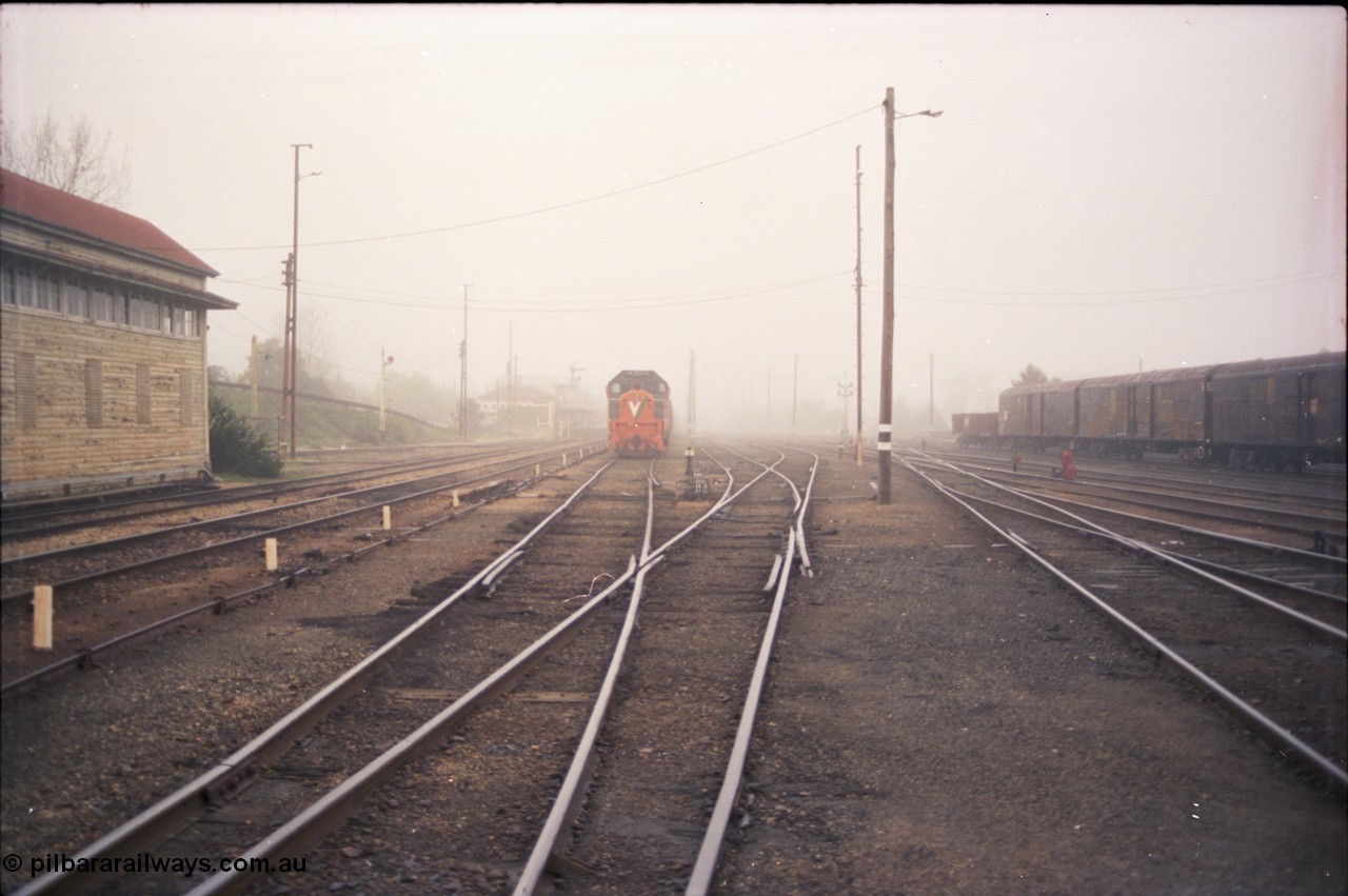 142-1-13
Benalla yard view, stabled broad gauge Wodonga goods train 9303 with V/Line X class X 48 Clyde Engineering EMD model G26C serial 75-795, Benalla signal box, station in background, very foggy, NSW louvre vans at right, track view.
Keywords: X-class;X48;Clyde-Engineering-Rosewater-SA;EMD;G26C;75-795;