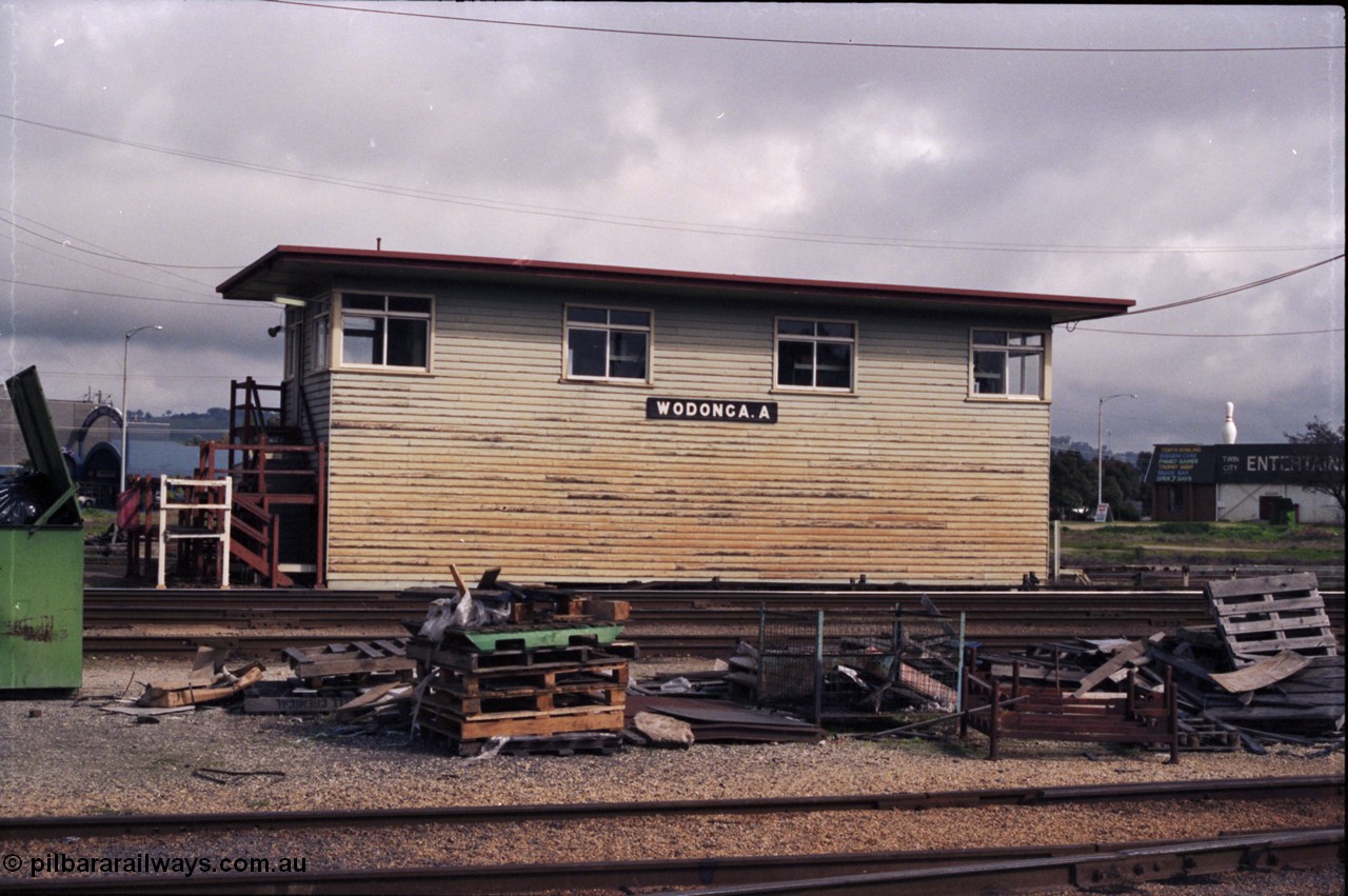 142-2-23
Wodonga station yard, signal box A, front elevation, load of pallets and rubbish in shot, staff exchange platform at the left of signal box.
