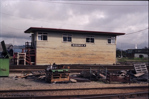 142-2-23
Wodonga station yard, signal box A, front elevation, load of pallets and rubbish in shot, staff exchange platform at the left of signal box.
