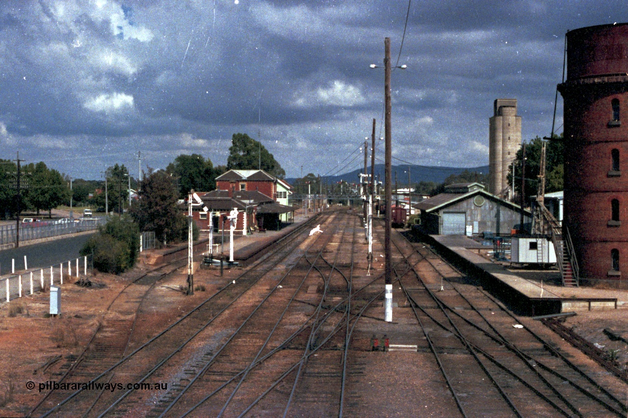 143-01
Wangaratta station yard overview looking south from footbridge, the broad gauge down Wahgunyah Special mixed train 'Stringybark Express' arrives and the signal man swaps electric staffs with the crew, the 18th century infrastructure clearly on display here, semaphore signal Post 20 is pulled off for departure, station building and platform, elevated signal box, signal posts and interlocking, goods shed and water tower.
