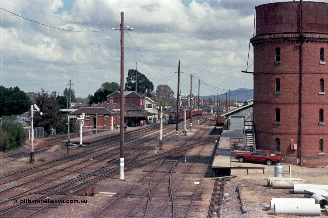 143-03
Wangaratta station yard overview looking south from footbridge, VR liveried Y class Y 133 Clyde Engineering EMD model G6B serial 65-399 brings the board gauge down Wahgunyah Special 'Stringybark Express' to a stop at the platform, the fully interlocked yard and 18th century infrastructure clearly on display here, semaphore signal Post 20 is pulled off for departure, station building and platform, elevated signal box, signal posts and interlocking, goods shed and water tower.
