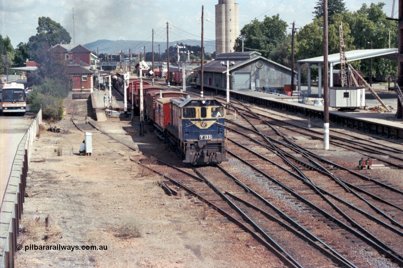 143-06
Wangaratta station yard overview looking south from footbridge, VR liveried Y class Y 133 Clyde Engineering EMD model G6B serial 65-399 departs the platform in the still fully interlocked yard with the broad gauge down 'Stringybark Express' mixed train to Wahgunyah, the K crossing for Siding A having only recently removed, signal post, goods shed, silos and yard crane.
Keywords: Y-class;Y133;Clyde-Engineering-Granville-NSW;EMD;G6B;65-399;