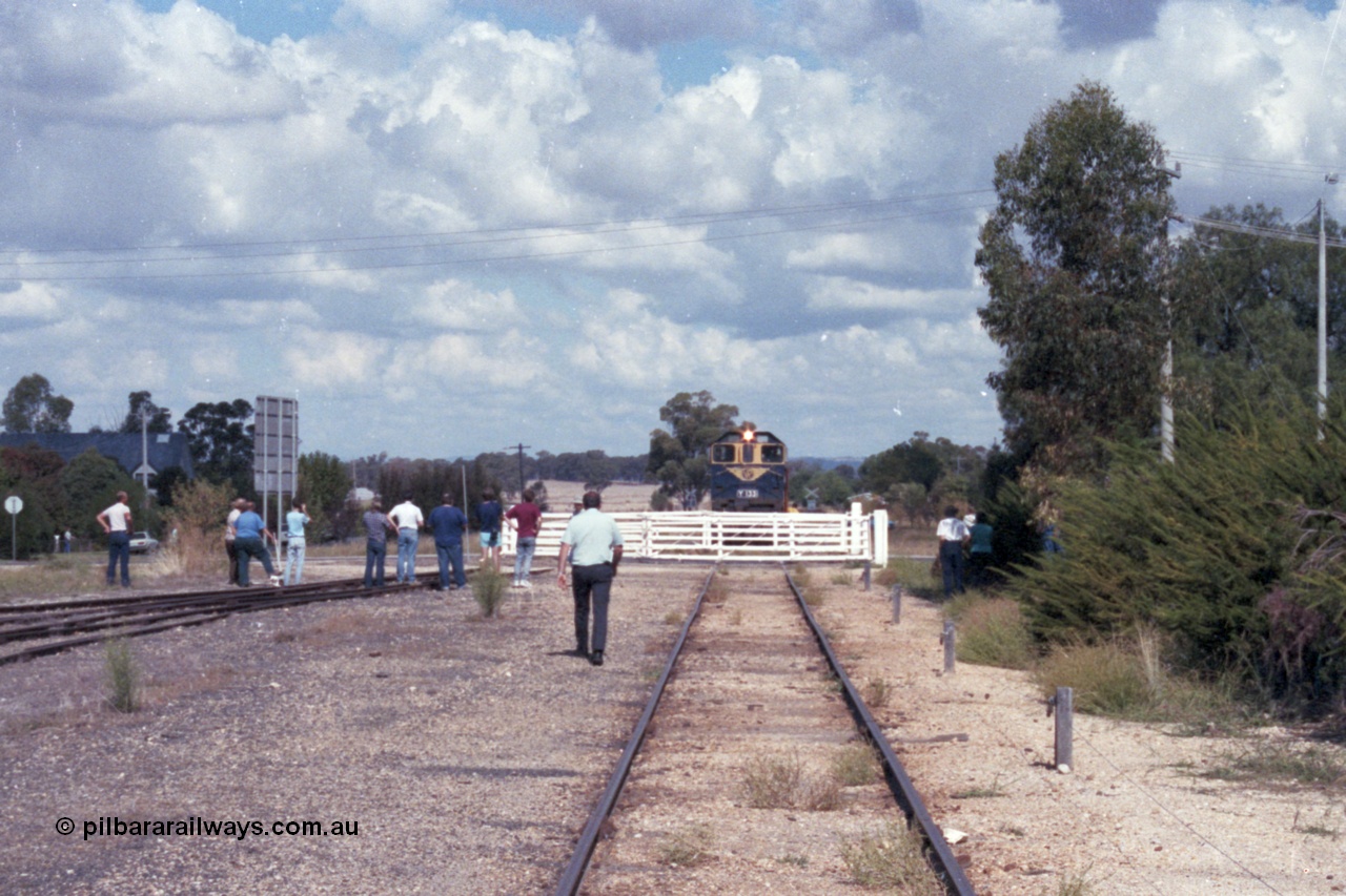 143-19
Rutherglen yard view, the signaller walks down to the hand operated swing gates protecting Howlong St to allow broad gauge VR liveried Y class Y 133 Clyde Engineering EMD model G6B serial 65-399 to cross with the down Wahgunyah mixed 'Stringybark Express' special.
