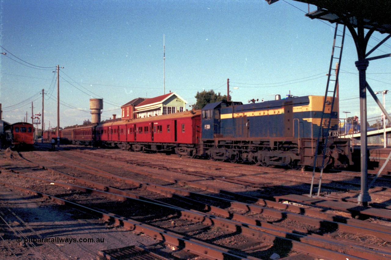 144-09
Wangaratta yard view, Victorian Railways liveried broad gauge Y class Y 133 Clyde Engineering EMD model G6B serial 65-399 holds the up Wahgunyah mixed special the 'Stringybark Express' in No. 2 Rd while V/Line rail tractor RT class RT 5 looks on from No. 5 Rd. The water tank in the background is the town water supply, the railways tank is just visible on the left edge of shot.
Keywords: Y-class;Y133;Clyde-Engineering-Granville-NSW;EMD;G6B;65-399;
