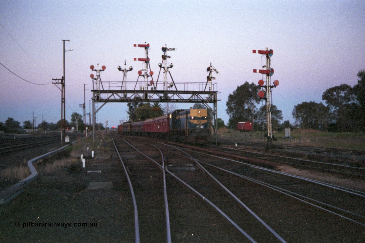 144-18
Benalla station yard overview looking north, signal gantry semaphore signal Post 28 pulled off, VR liveried broad gauge Y class Y 133 Clyde Engineering EMD model G6B serial 65-399 leads the up Wahgunyah 'Stringybark Express' mixed towards Benalla platform, a workman's W class four wheel sleeper 'bug hut' is in the background, semaphore signal Post 27 at right, signals and yard still intact and interlocked.
Keywords: Y-class;Y133;Clyde-Engineering-Granville-NSW;EMD;G6B;65-399;