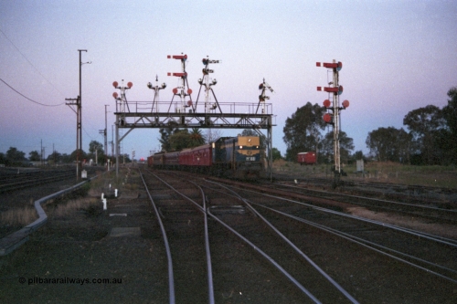 144-18
Benalla station yard overview looking north, signal gantry semaphore signal Post 28 pulled off, VR liveried broad gauge Y class Y 133 Clyde Engineering EMD model G6B serial 65-399 leads the up Wahgunyah 'Stringybark Express' mixed towards Benalla platform, a workman's W class four wheel sleeper 'bug hut' is in the background, semaphore signal Post 27 at right, signals and yard still intact and interlocked.
Keywords: Y-class;Y133;Clyde-Engineering-Granville-NSW;EMD;G6B;65-399;