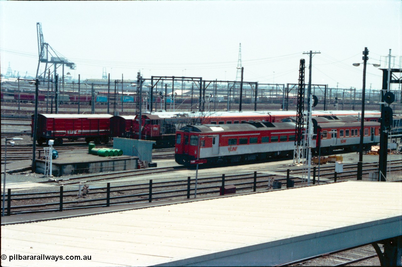 145-02
Spencer Street Station, Melbourne Yard overview towards Melbourne Port shows rail cars, passenger carriages and shunt loco with view across goods yard with DRC, MTH, D van and Y classes all present, Port of Melbourne container crane in distance.
