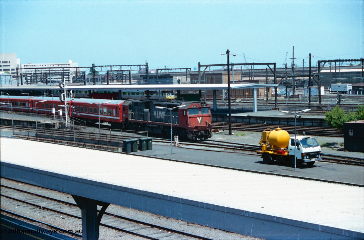 145-03
Spencer Street Station overview, broad gauge V/Line N class N 454 'City of Horsham' Clyde Engineering EMD model JT22HC-2 serial 85-1222 departs with a carriage set, a suburban Met coloured Comeng spark in the background, septic tank pump truck in foreground.
Keywords: N-class;N454;Clyde-Engineering-Somerton-Victoria;EMD;JT22HC-2;85-1222;